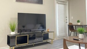 Een moderne woonkamer met een flatscreen televisie, een plafondventilator en een eethoek met stoelen en een tafel.