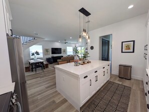 A modern kitchen with a central island, dining area, and a living room with a TV. - THE TOGETHER PLACE 2 (naples)