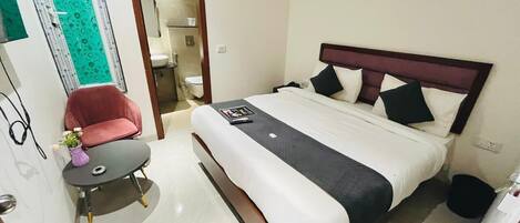 Una habitación de hotel con una cama, una mesita con una silla, un baño y una puerta que da a otra habitación.