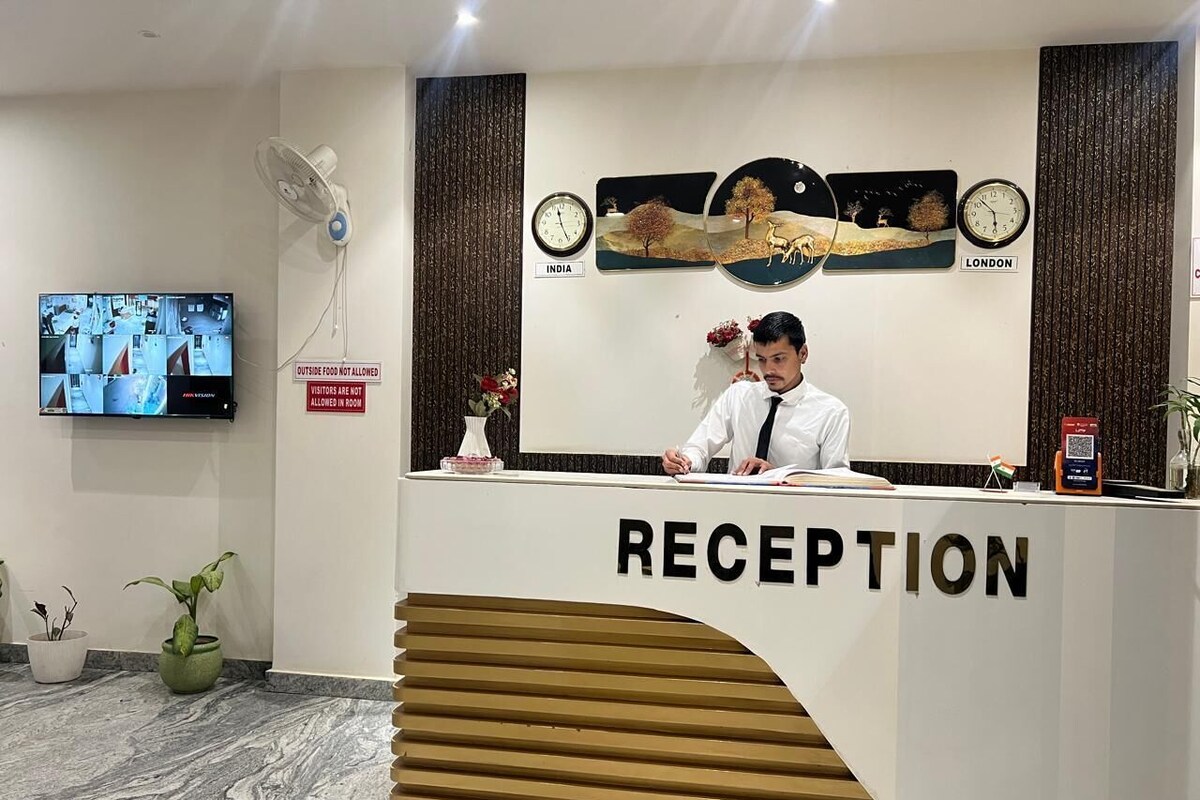 A reception desk with a sign reading 'RECEPTION,' a clock, and a wall-mounted TV displaying a security camera feed.