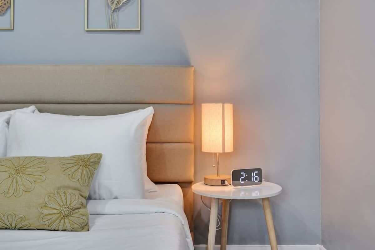 A neatly made bed with a pillow, a bedside lamp, and a digital clock displaying the time.