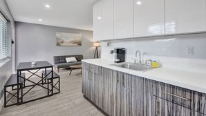 A modern kitchen with white cabinets, a marble countertop, and a dining area with a table and chairs. - 906 North Riverside Dr (Pompano Beach)