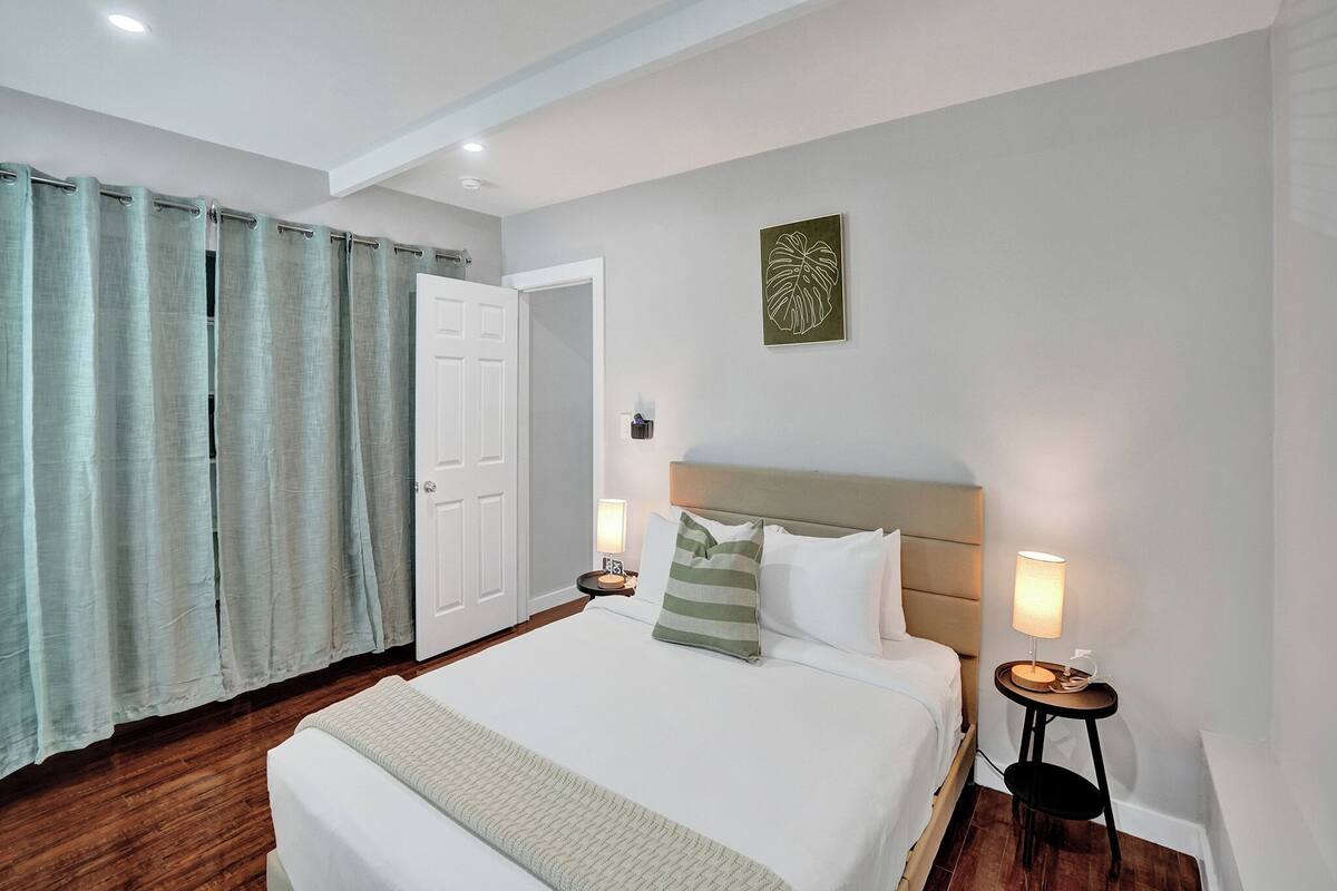 A bedroom with a bed, bedside tables, a door, and a wall-mounted artwork.
