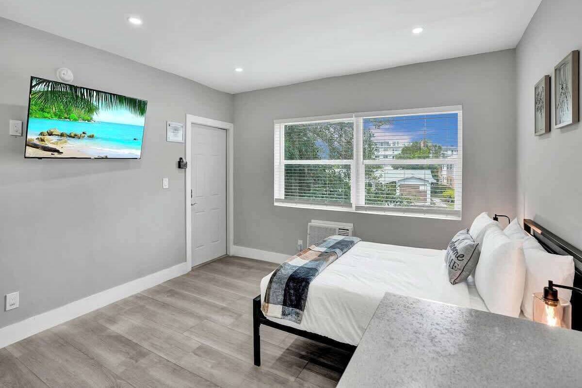 A bedroom with a bed, a TV, a window with a city view, and a door.