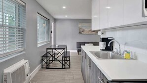 A modern kitchen with white cabinets, a black dining table, and a large window with blinds. - 906 North Riverside Dr (Pompano Beach)