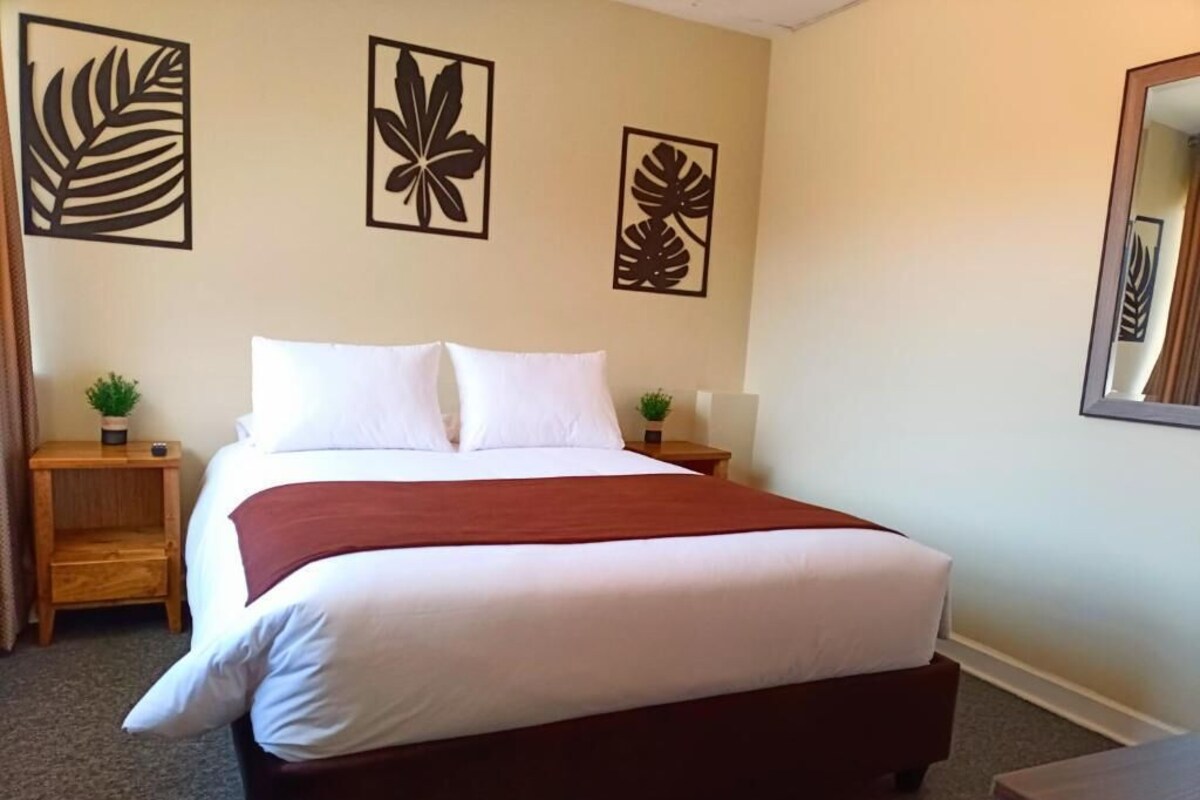 A hotel room with a bed, a nightstand with a plant, and wall art.