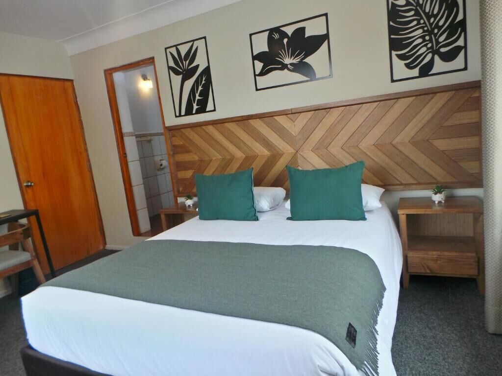 Ein Hotelzimmer mit einem Bett, zwei grünen Kissen, einem Holzkopfende und Wandbildern.