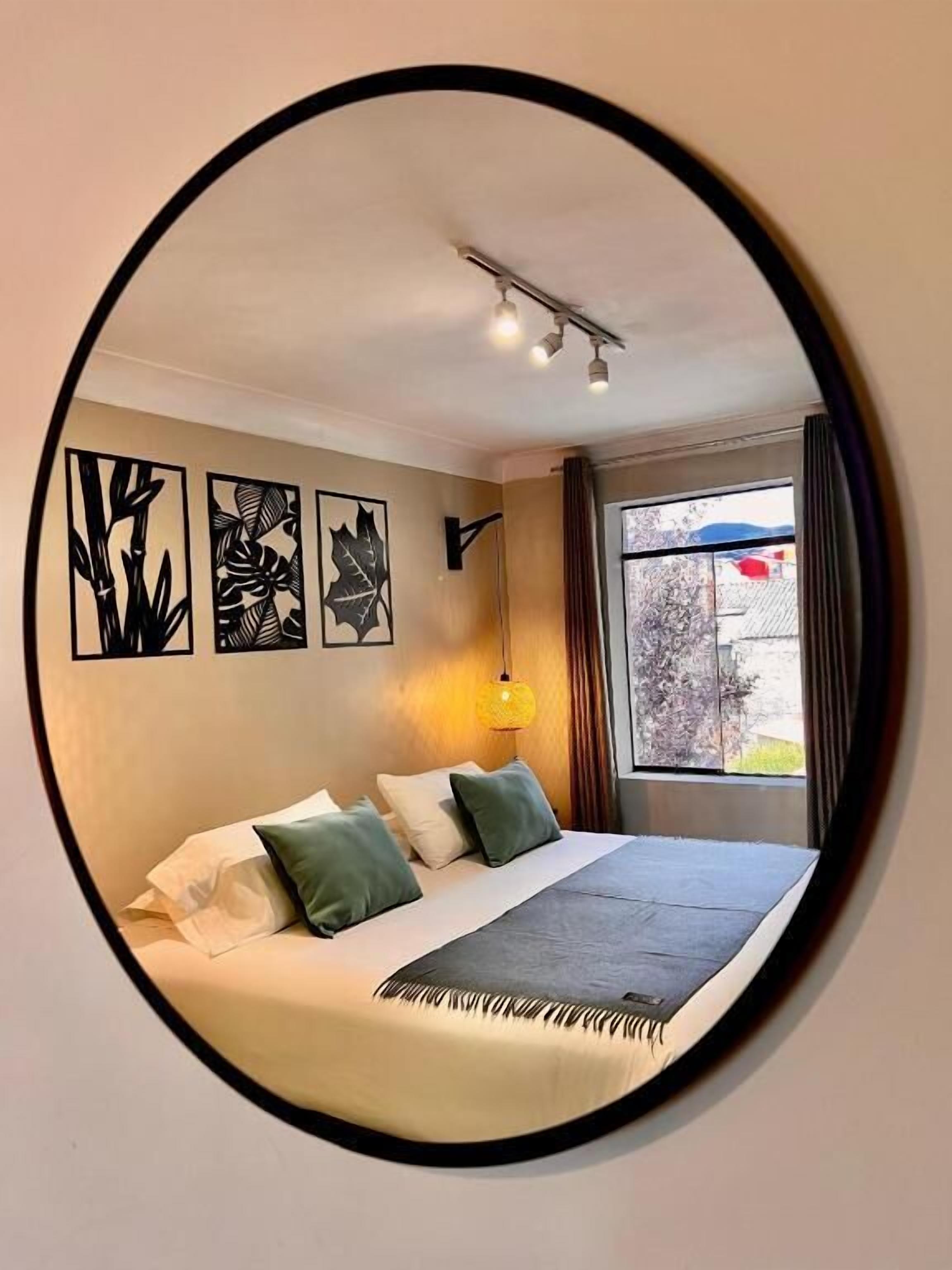Une chambre à coucher avec un lit, des oreillers, une lampe fixée au mur et des œuvres d’art.