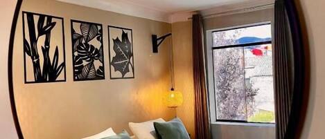 Une chambre à coucher avec un lit, des oreillers, une lampe fixée au mur et des œuvres d’art.
