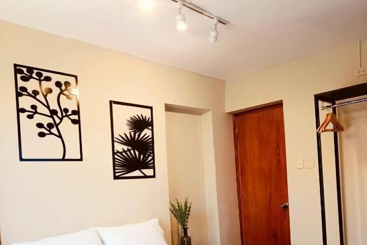 A bedroom with a bed, a nightstand, a plant, and artwork on the wall.
