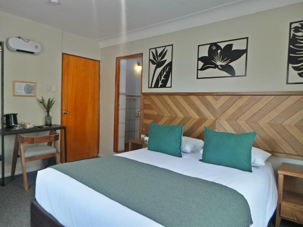 A hotel room with a bed, a desk, a chair, a wooden headboard, and wall art.