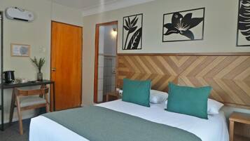 A hotel room with a bed, a desk, a chair, a wooden headboard, and wall art.