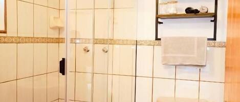 Un baño con cabina de ducha de vidrio, inodoro, perchero y un cubo de basura.