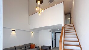 A modern living room with a sofa, ottoman, and a wooden staircase. - My Sunset Suite Apartments (Kuşadası)