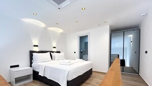 A modern bedroom with a bed, bedside tables, and a wooden bench. - My Sunset Suite Apartments (Kuşadası)