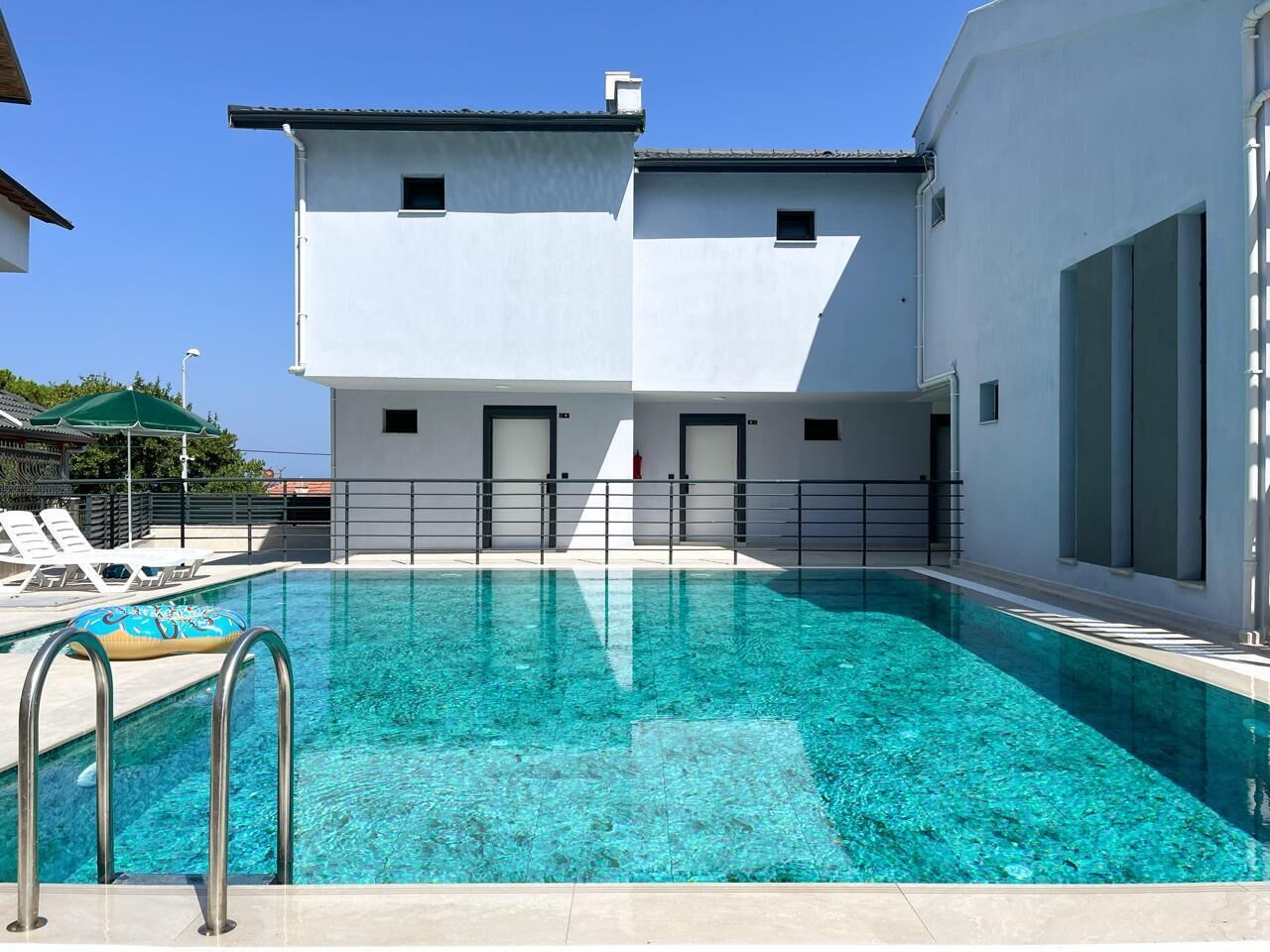 Una piscina con acqua cristallina, circondata da un edificio bianco con tetto piatto e un balcone.