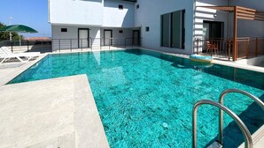 A swimming pool with a clear blue water, surrounded by a modern building with a flat roof and a balcony. - My Sunset Suite Apartments (Kuşadası)