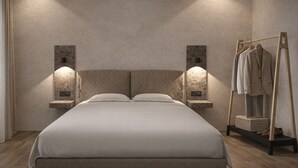 A bed with a headboard, two wall-mounted lights, a wooden floor, and a clothing rack with a mannequin. - CAVO III Luxury Rooms (Chania)