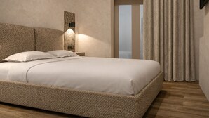 A bedroom with a large bed, a wall-mounted light, a door, and a curtain. - CAVO III Luxury Rooms (Chania)