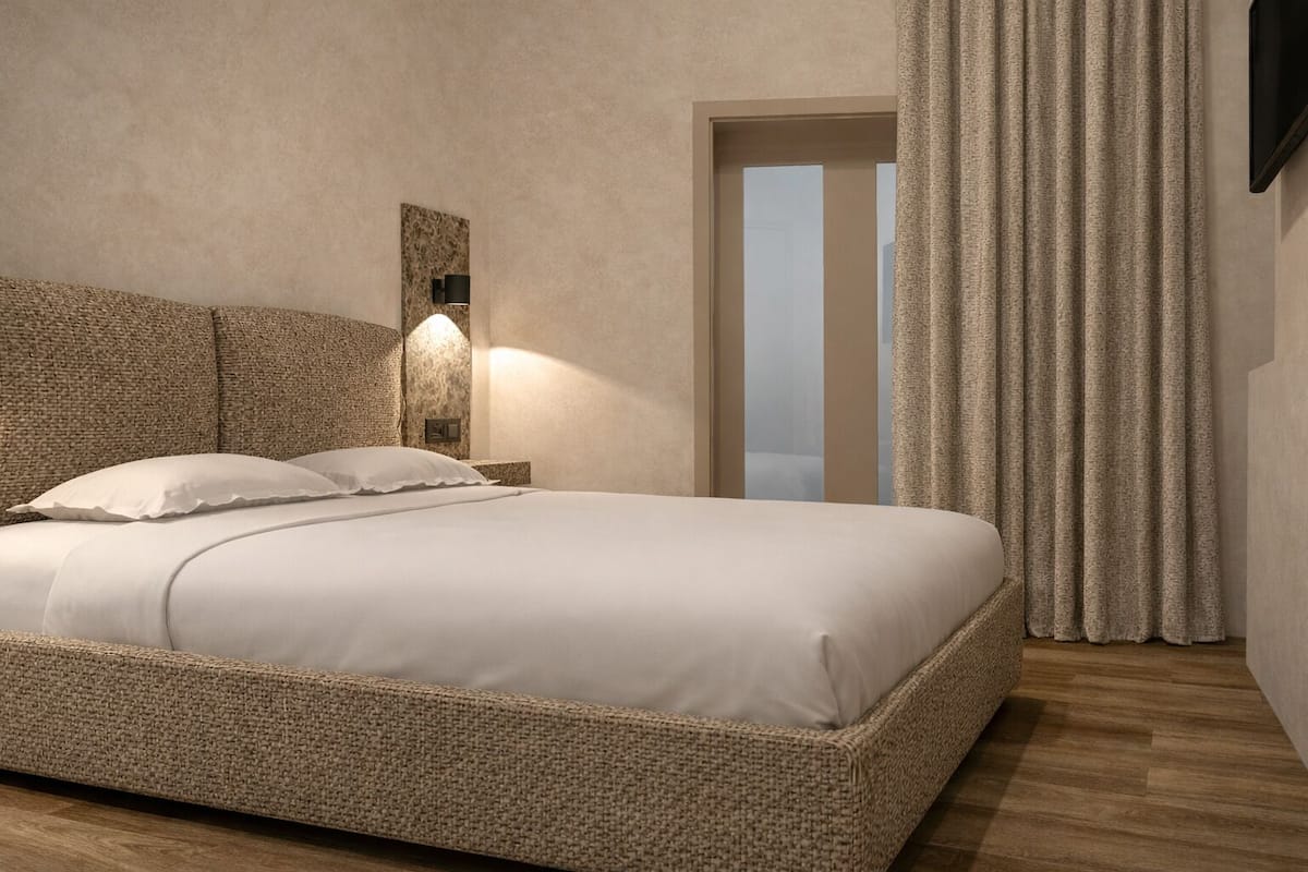 A bedroom with a large bed, a wall-mounted light, a door, and a curtain.