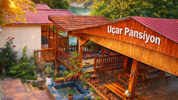 Eine Holzhütte mit einem Schild, auf dem 'Ucair Pansiyon' steht, und einem kleinen Gartenbereich mit Blumentöpfen.