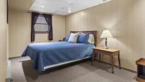 A single bed with a blue quilt, a bedside table with a lamp, and a window with curtains. - Lakefront Home w/ Private Apartment | Sleeps 12 | Boat Slip Available (Branson West)