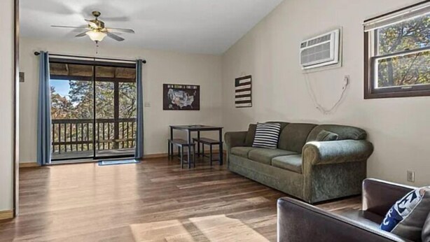 Un salon doté d’un plancher en bois, d’un ventilateur de plafond, d’un canapé, d’une table à manger et d’une porte-fenêtre coulissante donnant sur un balcon.