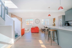 A modern kitchen with a bar area, a red accent chair, and a large wall clock. - Stylish 3BR Wimbledon | Roof Terrace & Parking (Greater London)