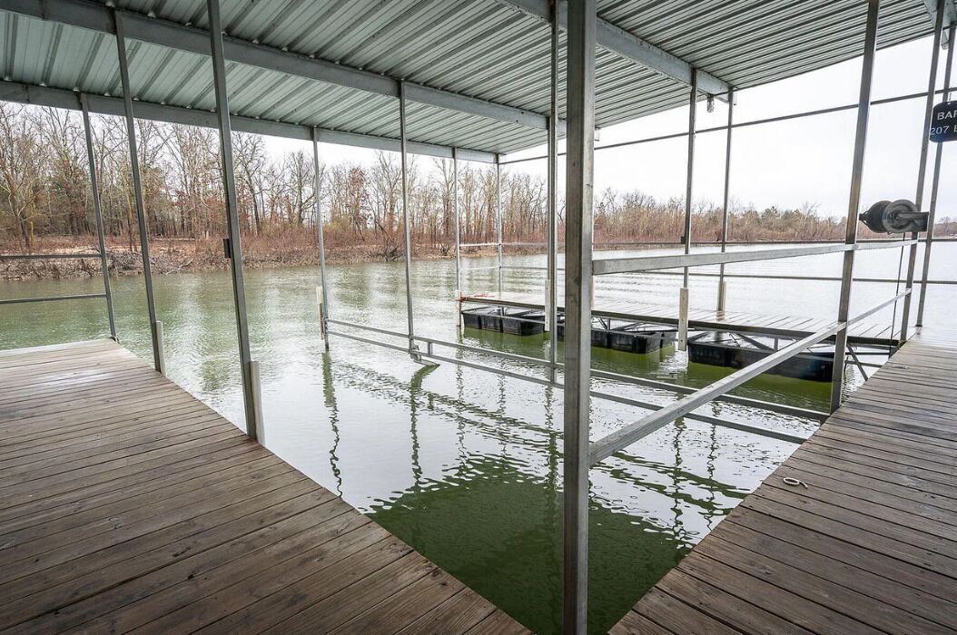 A covered dock area with a view of a water body and trees in the background.