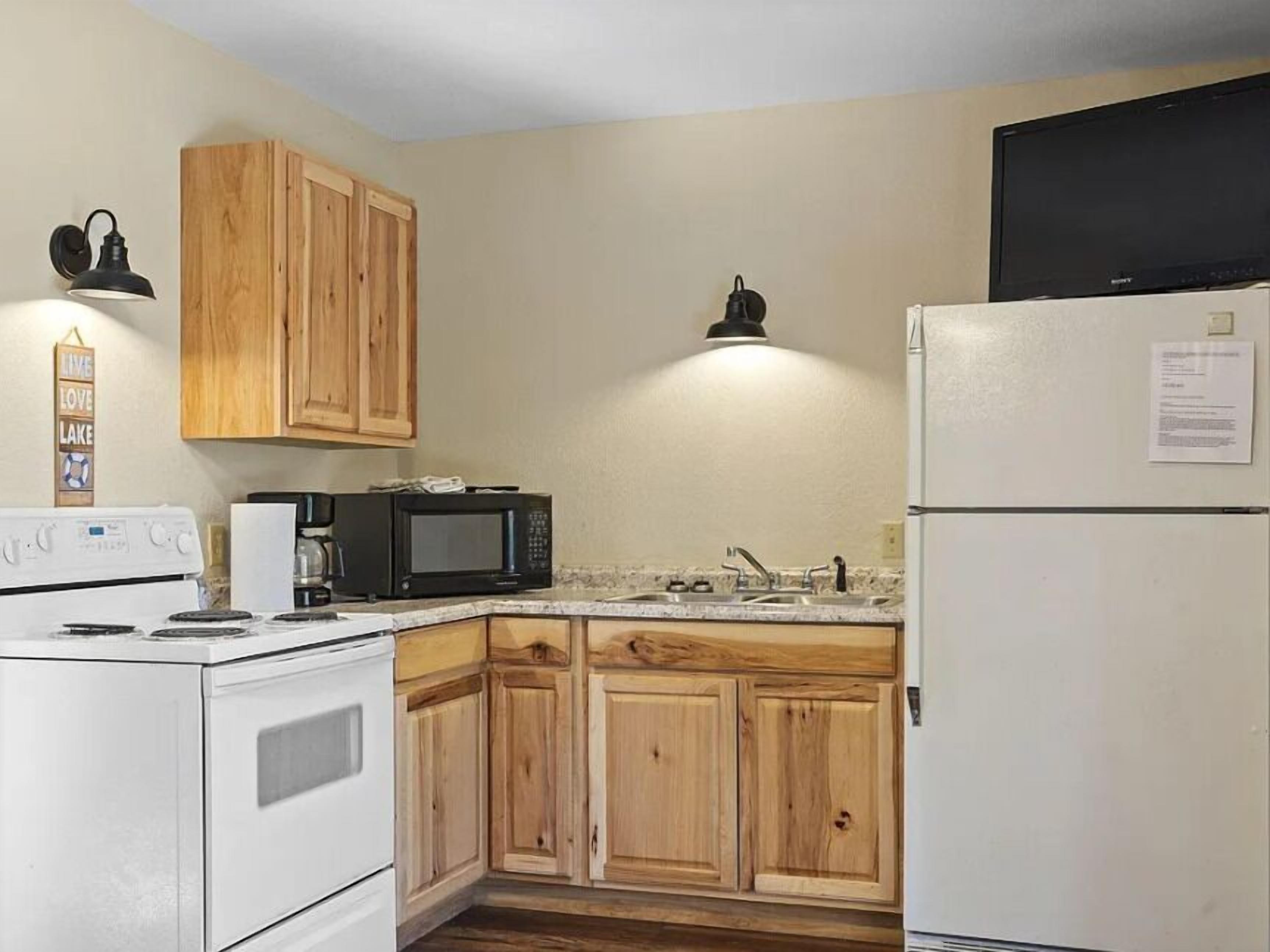 A kitchen with wooden cabinets, a white refrigerator, a microwave, a stove, and a black TV on top of the fridge.