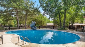 Una piscina con tobogán, rodeada de árboles y una cerca.