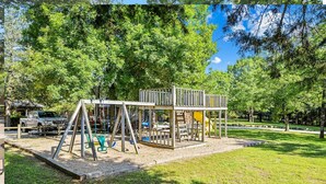 Un parque infantil con columpios y toboganes, rodeado de árboles y un cielo despejado.
