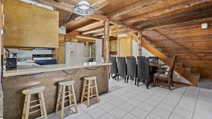 Una cocina rústica con barra, vigas de madera en el techo y una escalera que sube a un nivel superior.