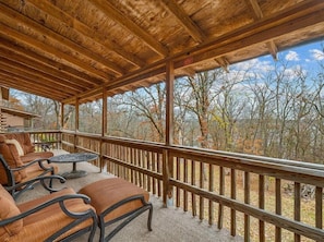 A covered outdoor seating area with wooden beams, a railing, and a view of trees.
