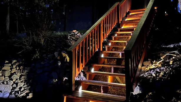 Una escalera de madera de varios niveles con barandillas, que conduce a un balcón con luces colgantes.