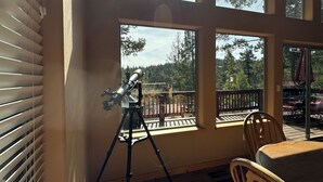 A room with a telescope on a tripod, large windows, a wooden table, and a patterned rug. - Stargazing Family Cabin, 2mi to Shopping & Hiking Trls. 2BR+Loft/Office, 2.5BA. (Cloudcroft)