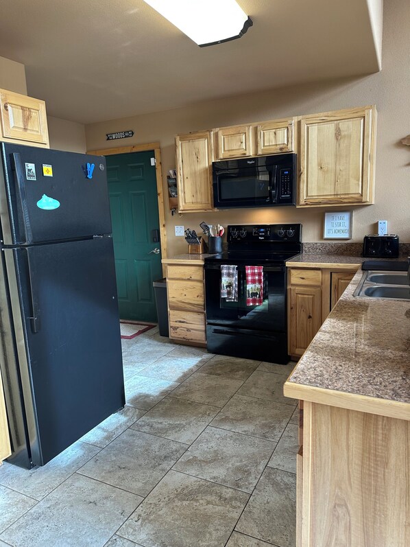 A kitchen with wooden cabinets, a black refrigerator, a microwave, a stove, and a countertop. - Stargazing Family Cabin, 2mi to Shopping & Hiking Trls. 2BR+Loft/Office, 2.5BA. (Cloudcroft)