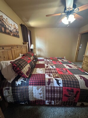 A bedroom with a wooden headboard, a quilted bedspread, a ceiling fan, and a painting on the wall. - Stargazing Family Cabin, 2mi to Shopping & Hiking Trls. 2BR+Loft/Office, 2.5BA. (Cloudcroft)