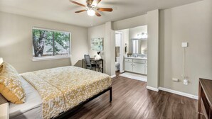 Une chambre avec un lit, un ventilateur de plafond, une fenêtre donnant sur un beau paysage, un bureau et une salle de bain avec un lavabo et un miroir.