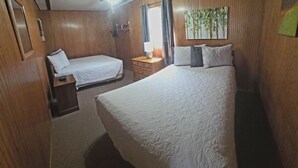 Een hotelkamer met twee bedden, houten lambrisering, een nachtkastje met lamp en een schilderij aan de muur.