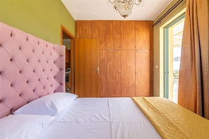 A bedroom with a tufted headboard, a wooden wardrobe, a bed with white bedding, and a view through a window with curtains. - Adorable 1-bedroom apartment with AC in charming Rethymno (Rethymno)