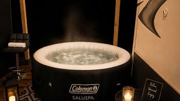 Ein Whirlpool mit Coleman-Logo, ein Massagesessel, eine Kerze und ein Schild mit der Aufschrift 'Relax Unwind Enjoy' in einem schwach beleuchteten Raum mit gemustertem Boden.