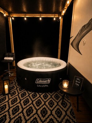 Ein Whirlpool mit Coleman-Logo, ein Massagesessel, eine Kerze und ein Schild mit der Aufschrift 'Relax Unwind Enjoy' in einem schwach beleuchteten Raum mit gemustertem Boden.