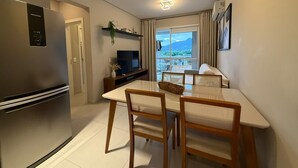 Cocina compacta con refrigerador, mesa de comedor con sillas, televisor y ventana con vistas.