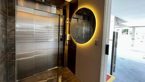 Un ascensor moderno con detalles metálicos, un espejo circular en la pared y una puerta que da a un espacio exterior.
