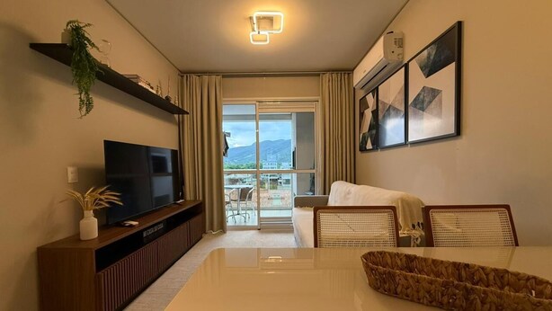 Habitación de hotel con televisión de pantalla plana, sofá, mesa de comedor, balcón con vistas y aire acondicionado instalado en la pared.
