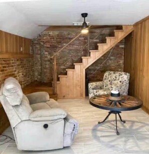 Ein Zimmer mit Backsteinwand, einer Holztreppe, einem Liegestuhl und einem runden Tisch.