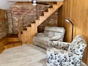Une pièce dotée d’un parquet à motifs en chevrons, d’un escalier en bois, d’un canapé recouvert d’un tissu à motifs de feuilles et d’un lampadaire.