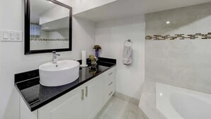 Ein modernes Badezimmer mit einem weißen Waschbecken, einer schwarzen Arbeitsplatte und einem großen Spiegel.