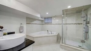 Ein modernes Badezimmer mit einer großen, weißen Badewanne, einer in Glas abgeschirmten Dusche und einem runden Waschbecken mit schwarzer Arbeitsplatte.